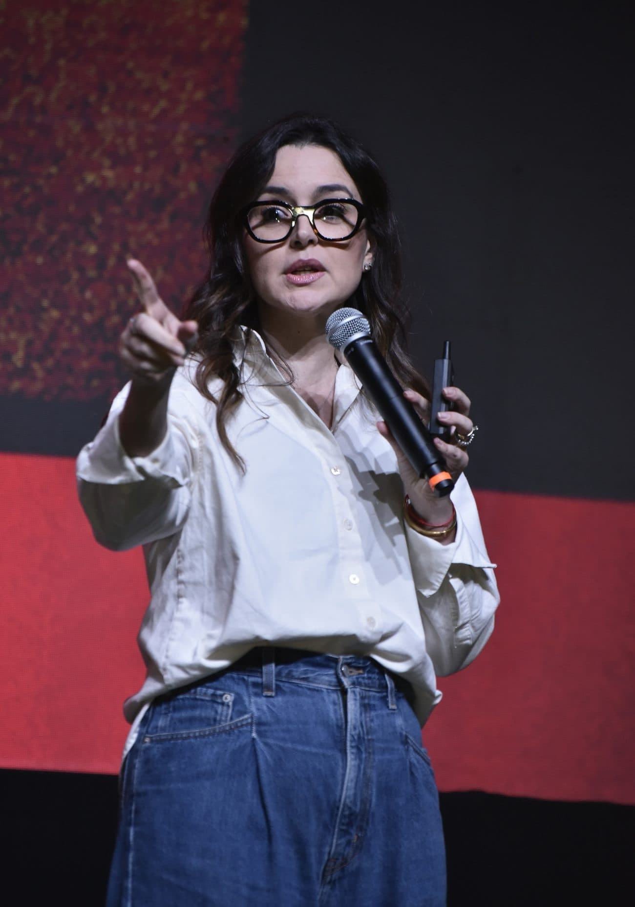 Izabela Anholett no palco, apontando enquanto fala ao microfone